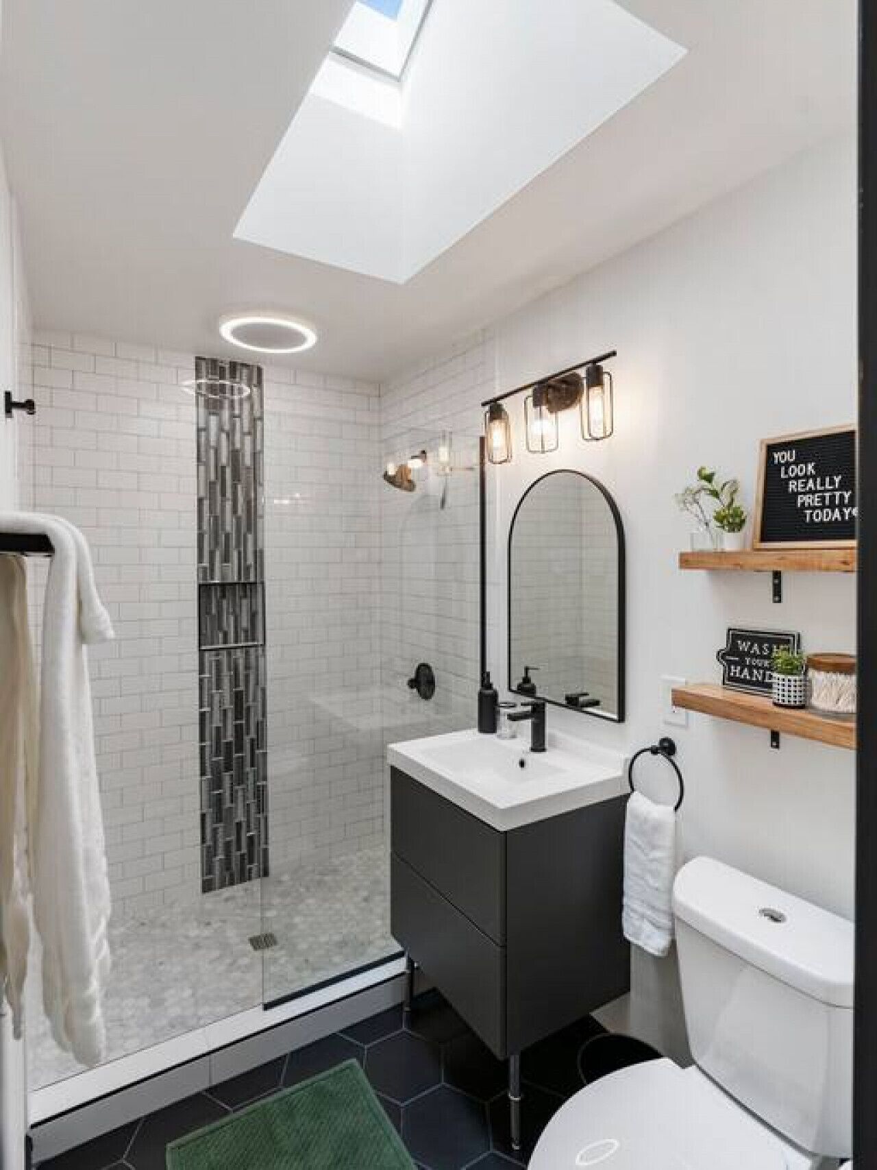 A modern bathroom with a skylight, a glass shower enclosure, a white sink, and a toilet.