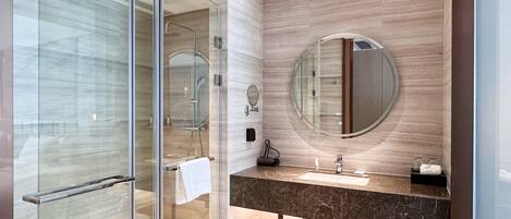 A modern bathroom with a glass shower enclosure, a round mirror, and a marble countertop.