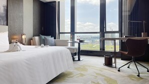 Camera d'albergo moderna con un letto grande, una scrivania, una sedia e vista sulla città attraverso ampie finestre.