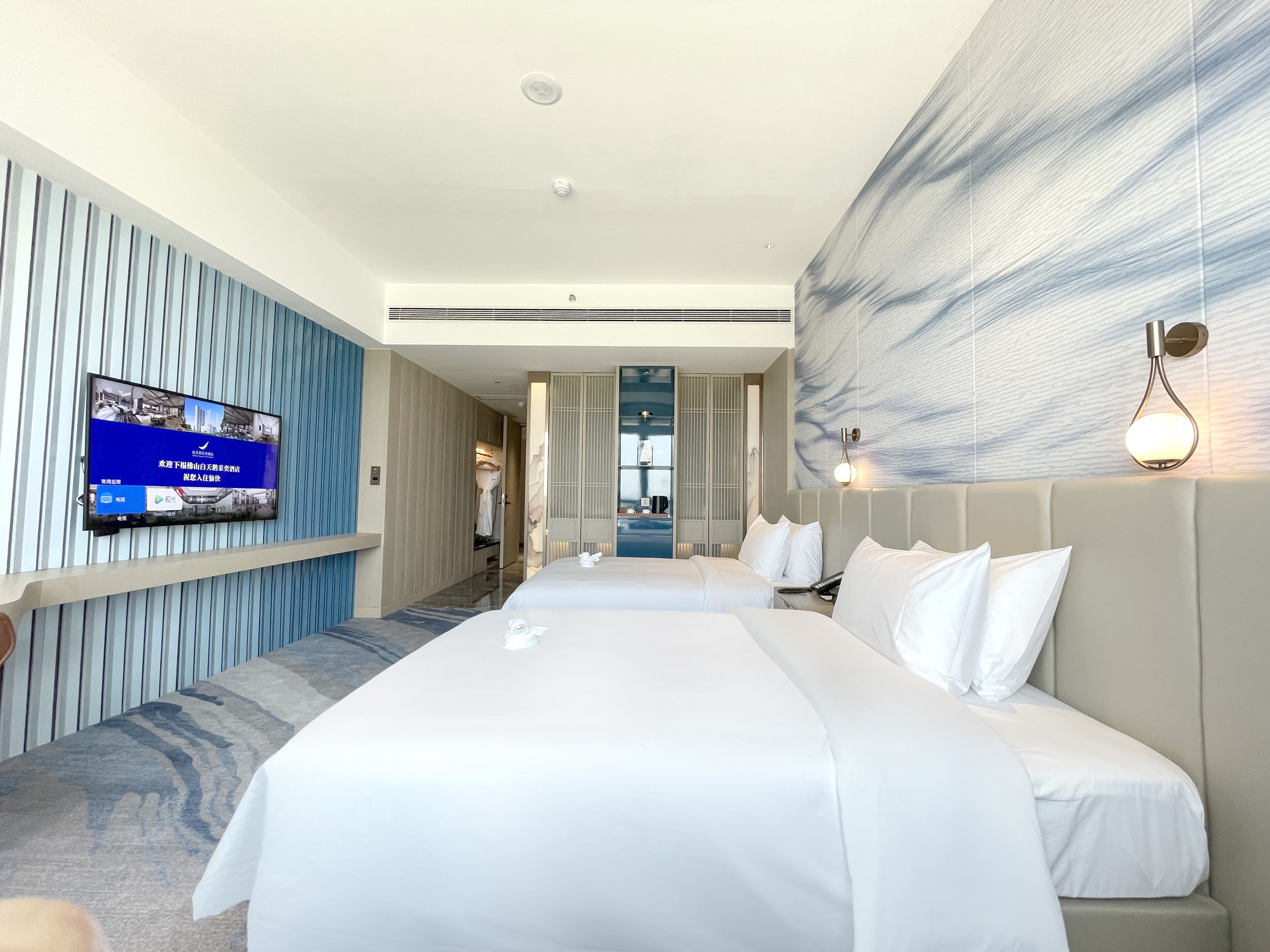 A hotel room with a large bed, a flat-screen TV mounted on the wall, and a modern design with a marble-like wall feature.