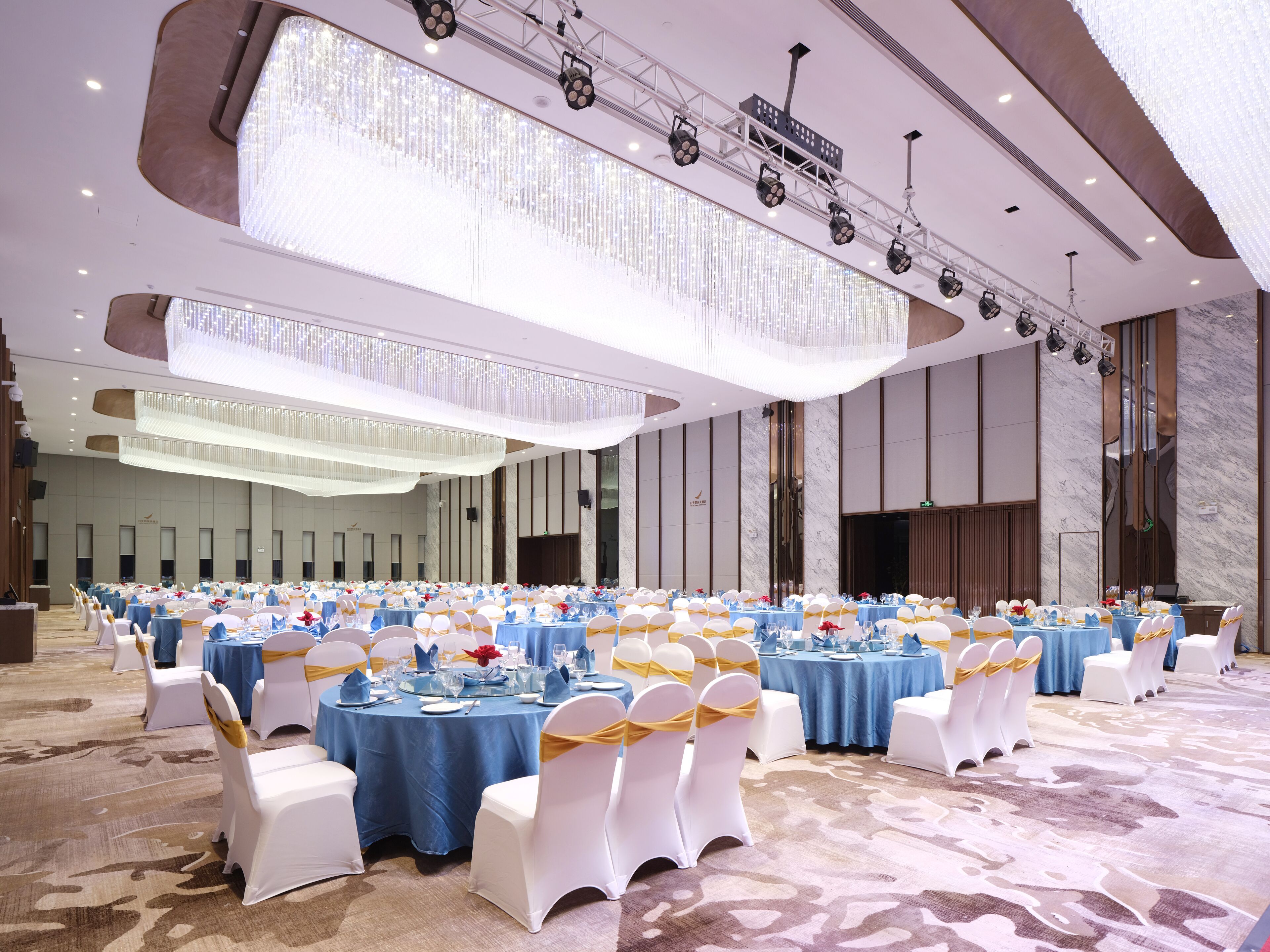 A large banquet hall with round tables, white chairs, and blue tablecloths.