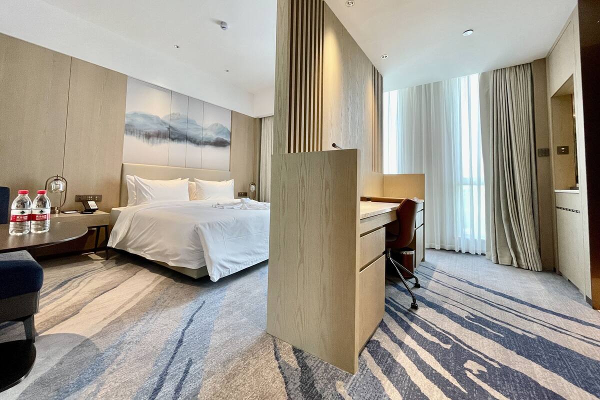 Una habitación de hotel con cama, escritorio, silla y un ventanal con cortinas.