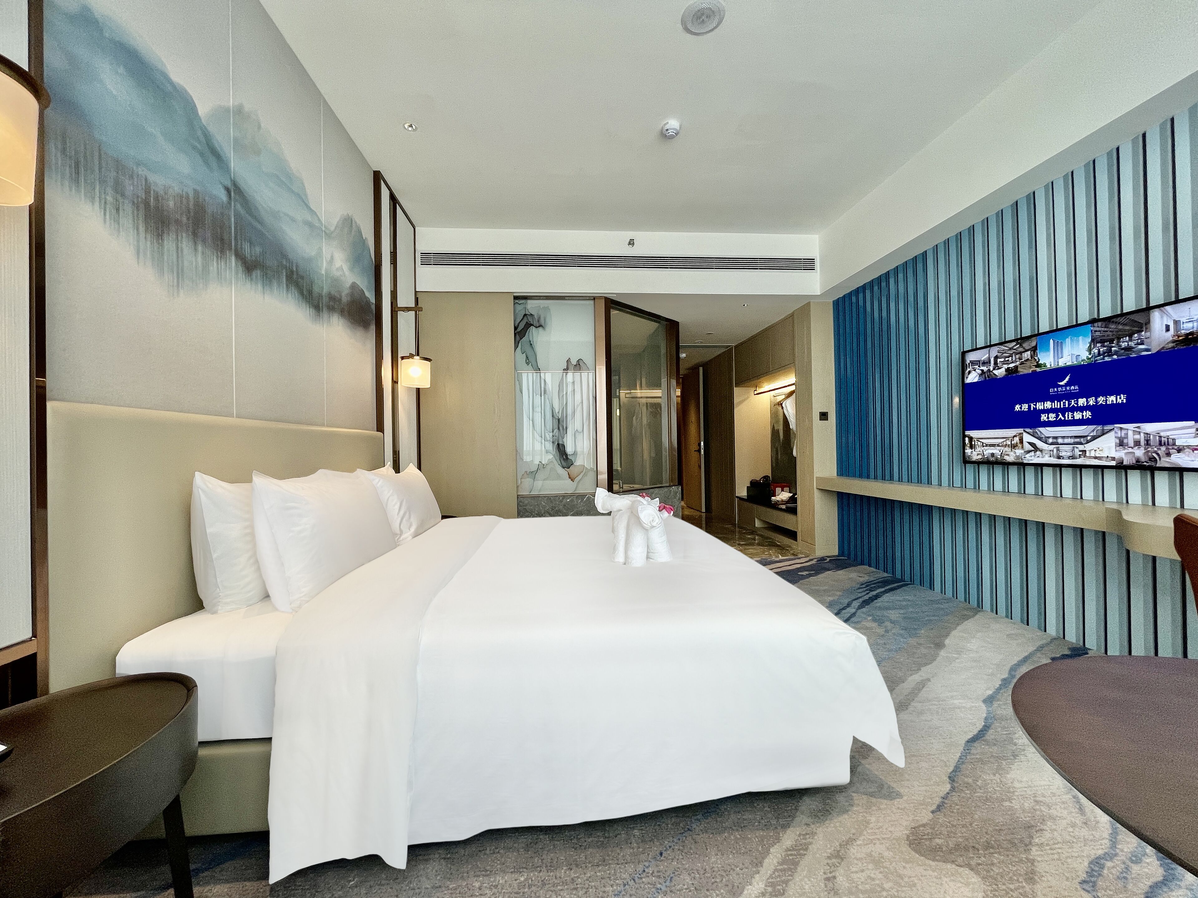 Une chambre d’hôtel moderne, dotée d’un grand lit, d’un téléviseur fixé au mur et d’une salle de bain visible à travers une porte ouverte.