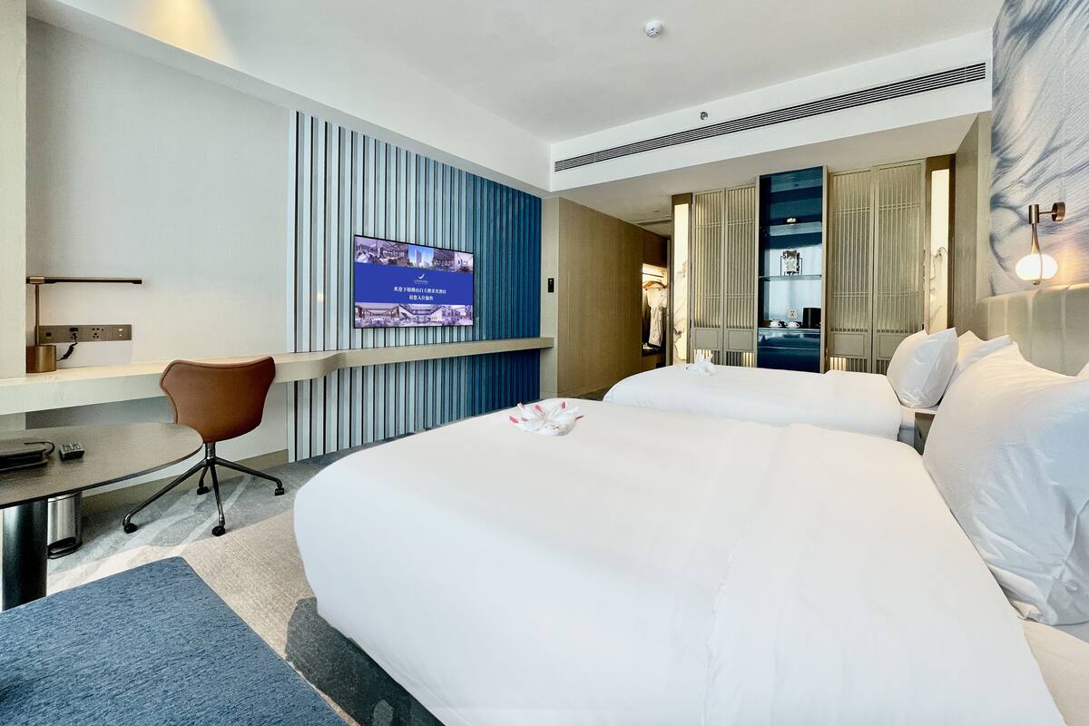 Habitación de hotel con una cama grande, un escritorio con silla, un televisor montado en la pared y un armario.
