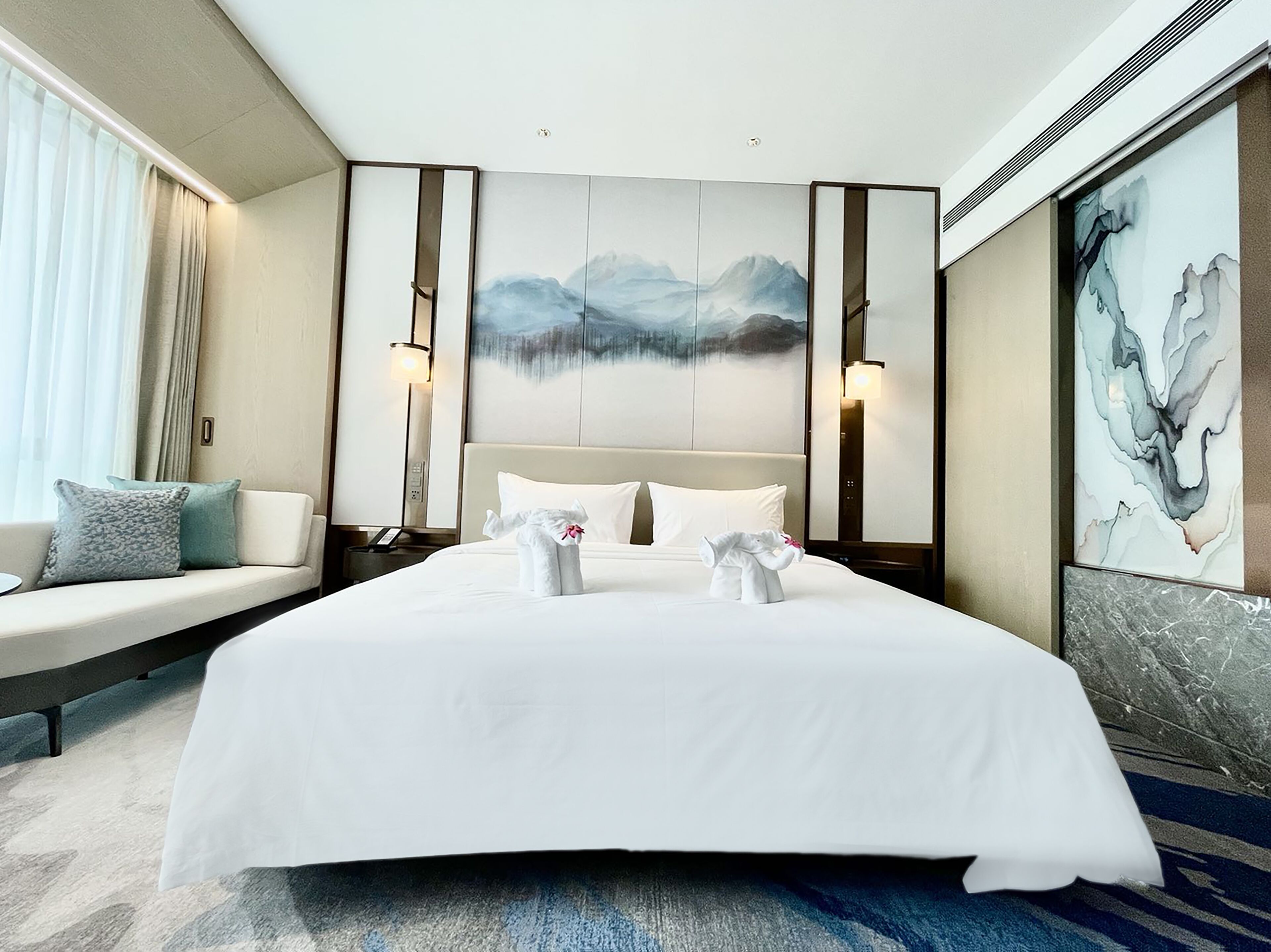 A hotel room with a large bed, a sofa, and a painting on the wall.