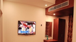 Une chambre d’hôtel équipée d’un téléviseur fixé au mur, d’une petite table en bois, d’une armoire et d’un miroir.