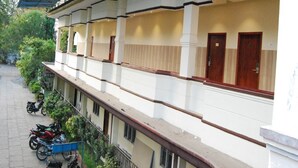 Un immeuble à plusieurs étages doté d’un balcon couvert, d’une rangée de portes au rez-de-chaussée et de quelques motos garées.