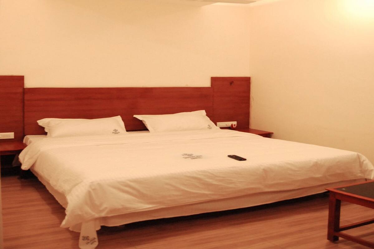 Hotellihuone, jossa on puinen sängynpääty, valkoinen päiväpeite ja yöpöytä.