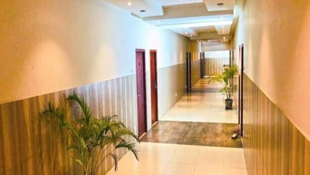 Un couloir d’hôtel avec un sol carrelé, des plantes en pot et des portes de chaque côté.