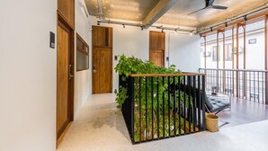 A hallway with wooden doors, a black metal railing with greenery, a ceiling fan, and a balcony with a chair. - U Chaikhong (Chiang Khan)