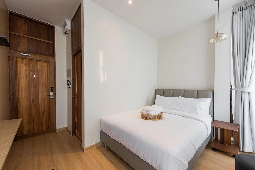 A bedroom with a bed, a wooden wardrobe, a small table, and a hanging light fixture.