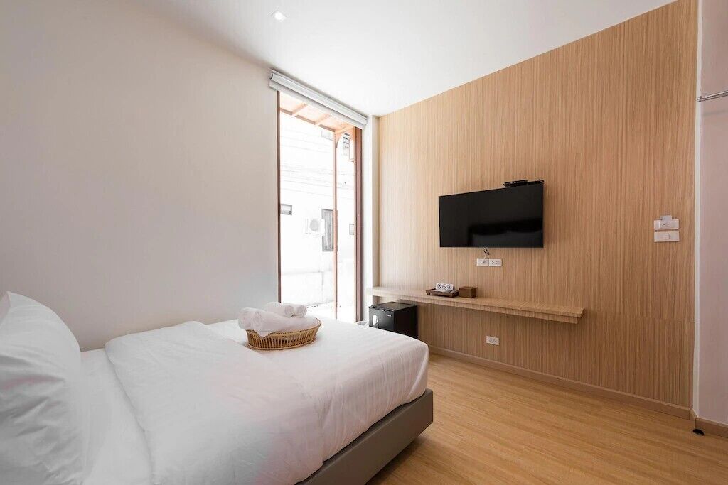 A modern hotel room with a bed, a television mounted on the wall, and a wooden panel wall.