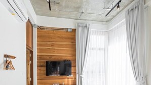 A modern hotel room with a wooden accent wall, a flat-screen TV, a bed with a basket of towels, and a black leather chair. - U Chaikhong (Chiang Khan)
