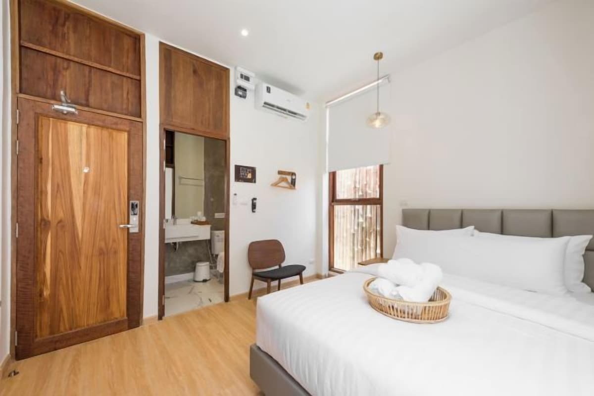 A bedroom with a bed, a wooden wardrobe, a chair, and a window with curtains.