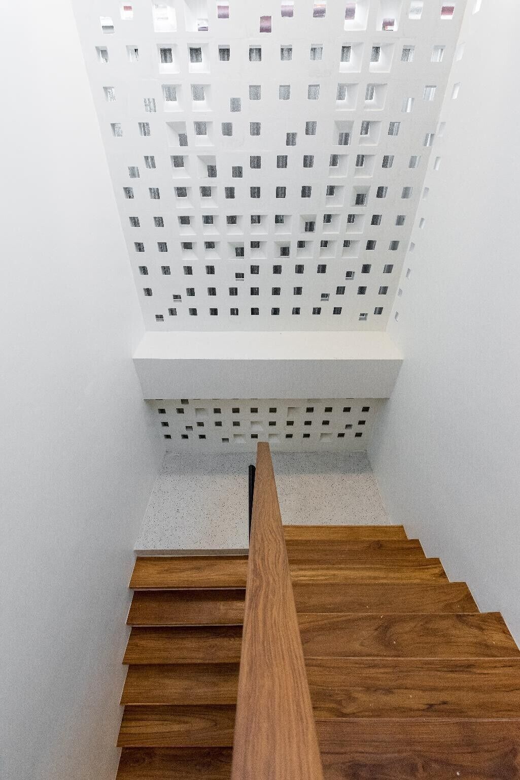 Un escalier en bois, avec un mur blanc et un plafond perforé.