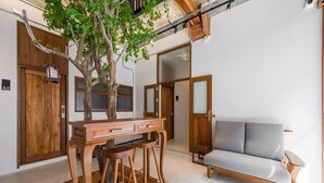A modern interior with a wooden desk, two stools, a grey sofa, and a tree. - U Chaikhong (Chiang Khan)
