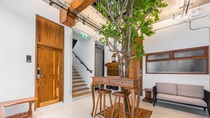A reception area with a wooden desk, two stools, a bench, a sofa, a staircase, and a tree. - U Chaikhong (Chiang Khan)