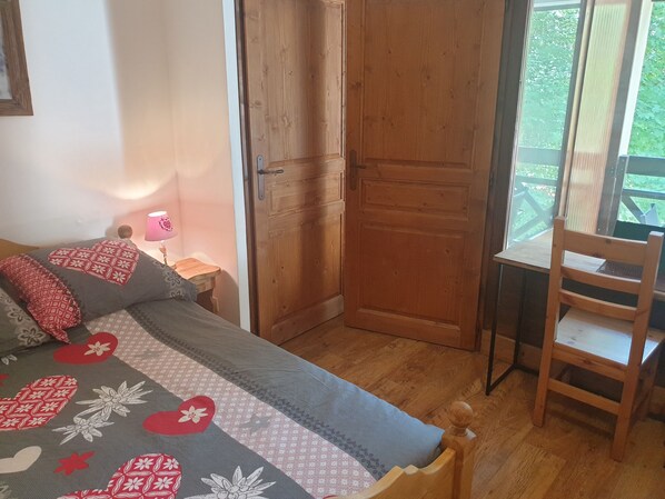 Un dormitorio con cama, una puerta de madera, una silla y una ventana con vista a follaje.