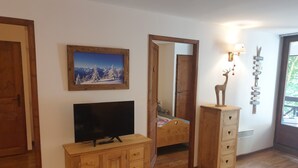 A room with a wooden cabinet, a television, a bed, a mirror, and a wall-mounted sign with names. - High quality apartment in the heart of the French Alps - 5 minutes from ski lift (Brides-les-Bains)