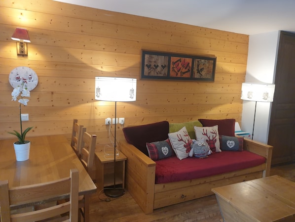 A cozy wooden interior with a wooden sofa, a dining table, chairs, and a potted orchid. - High quality apartment in the heart of the French Alps - 5 minutes from ski lift (Brides-les-Bains)