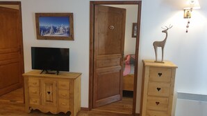 A room with a wooden cabinet, a television, a wooden door, and a wall-mounted lamp. - High quality apartment in the heart of the French Alps - 5 minutes from ski lift (Brides-les-Bains)