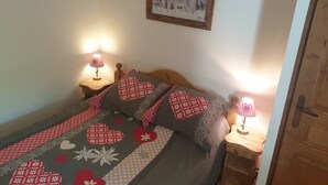 A cozy bedroom with a wooden bed, a patterned blanket, two bedside lamps, and a framed picture on the wall. - High quality apartment in the heart of the French Alps - 5 minutes from ski lift (Brides-les-Bains)
