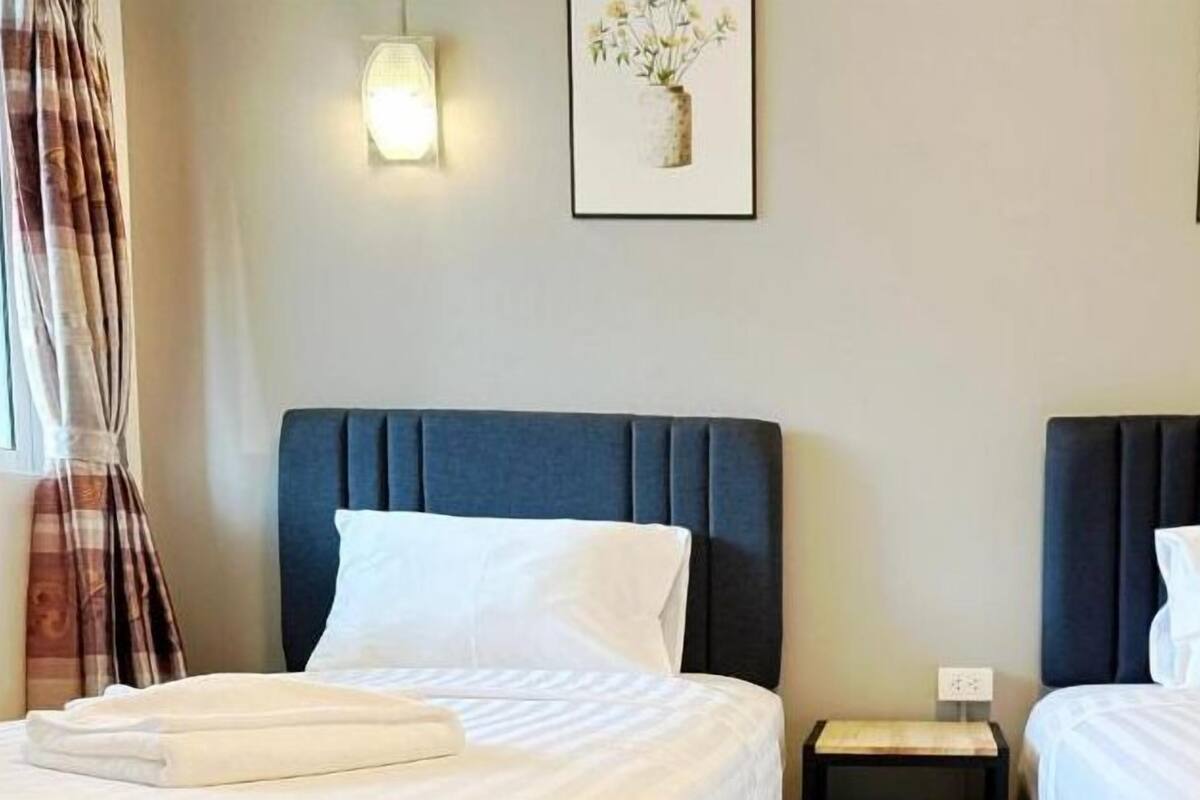 Habitación de hotel con dos camas, cada una con cabecero oscuro y ropa de cama blanca. Hay dos lámparas fijadas a la pared y dos cuadros enmarcados sobre las camas.