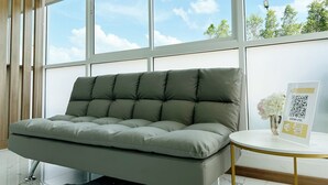 Una habitación moderna con un sofá gris, ventanas amplias, una mesa redonda blanca con un código QR y un pequeño florero con flores.