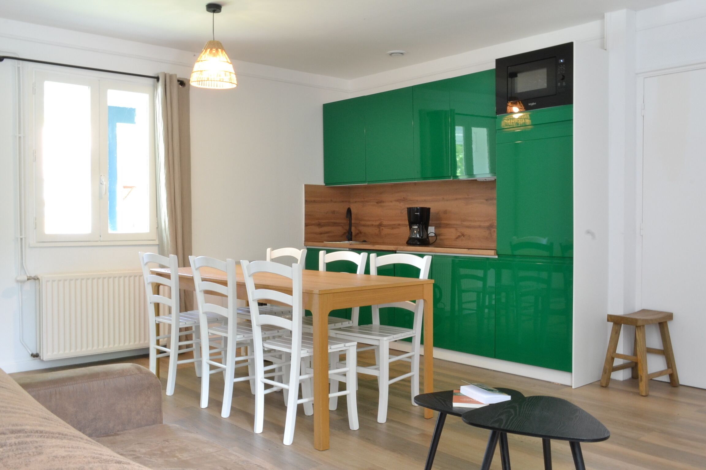A modern kitchen with green cabinets, a wooden table, and white chairs.