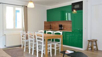 A modern kitchen with green cabinets, a wooden table, and white chairs.