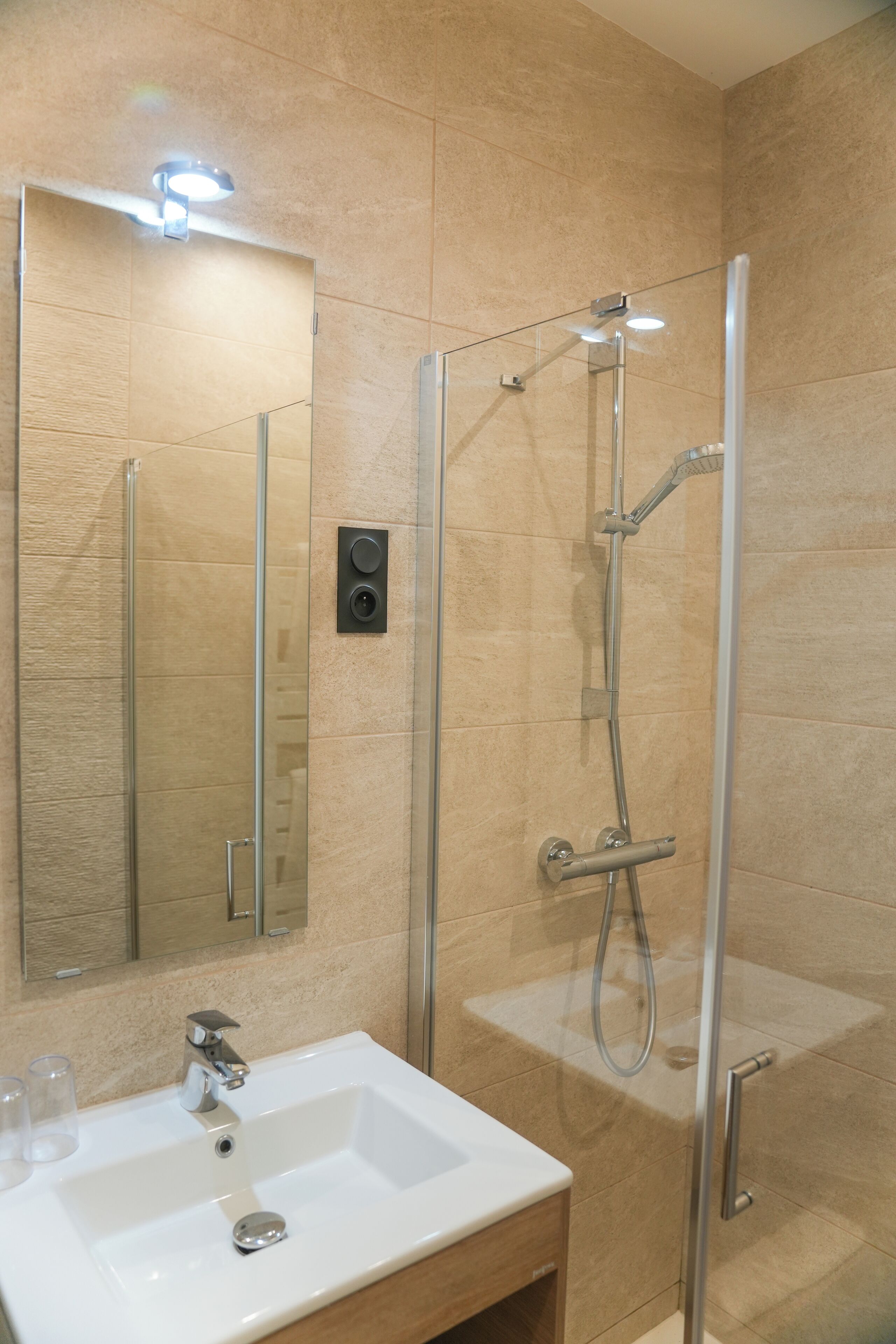 Een moderne badkamer met een douchecabine van glas, een witte wastafel en een spiegel.