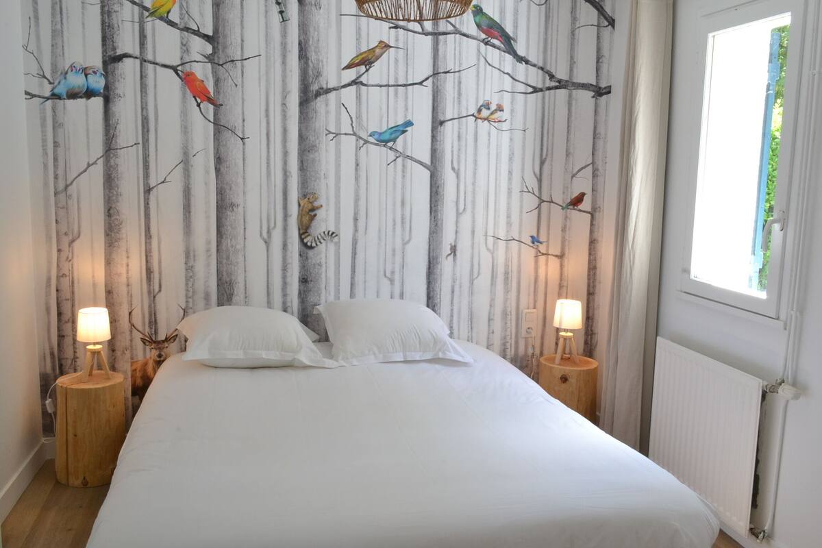Ein Schlafzimmer mit einem Bett, zwei Nachttischen mit Lampen, einem Fenster und einer Wand mit einem Vogelgemälde.