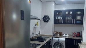 A compact kitchen with a stainless steel refrigerator, a built-in washing machine, and dark cabinets. - Apartment rental at agadir marina, إجار شقة بمارينا أكادير (Agadir)
