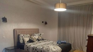 A bedroom with a bed, bedside tables, a desk, a chair, and a hanging light fixture. - Apartment rental at agadir marina, إجار شقة بمارينا أكادير (Agadir)