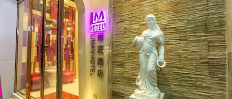 A hotel entrance with a glass facade, a neon sign, and a statue on the wall.