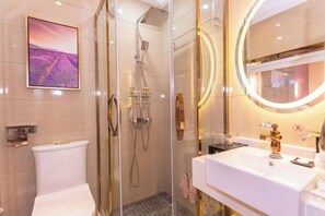 A modern bathroom with a glass-enclosed shower, a white sink with a gold faucet, and a framed picture on the wall.