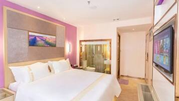Hotelkamer met een groot bed, een televisie, een badkamer met een douchecabine van glas en een roze muur.