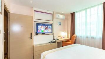A hotel room with a bed, a desk with a computer monitor, a chair, and a window with curtains.