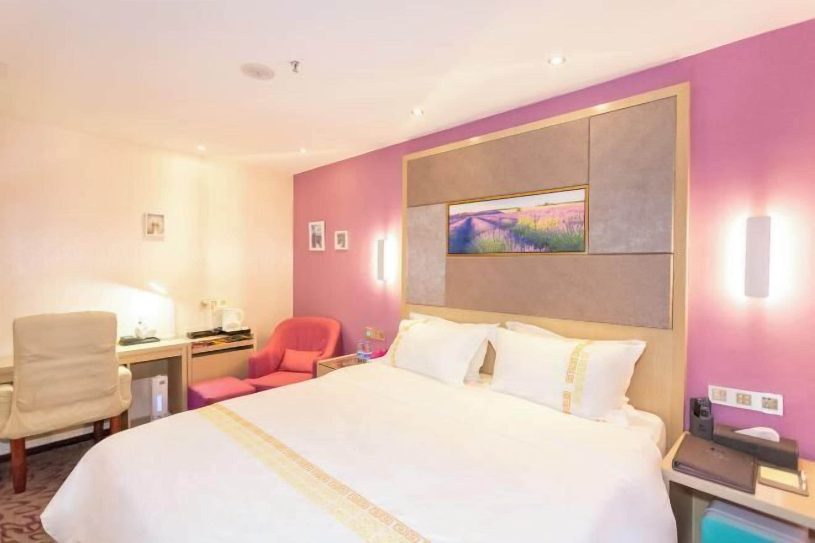 Quarto de hotel com uma cama grande, uma escrivaninha, uma cadeira e uma mesinha de cabeceira com abajur.