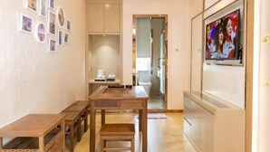 A hallway with a wooden table and chairs, a cabinet, and a television mounted on the wall. - Liman Hotel (Guangzhou)