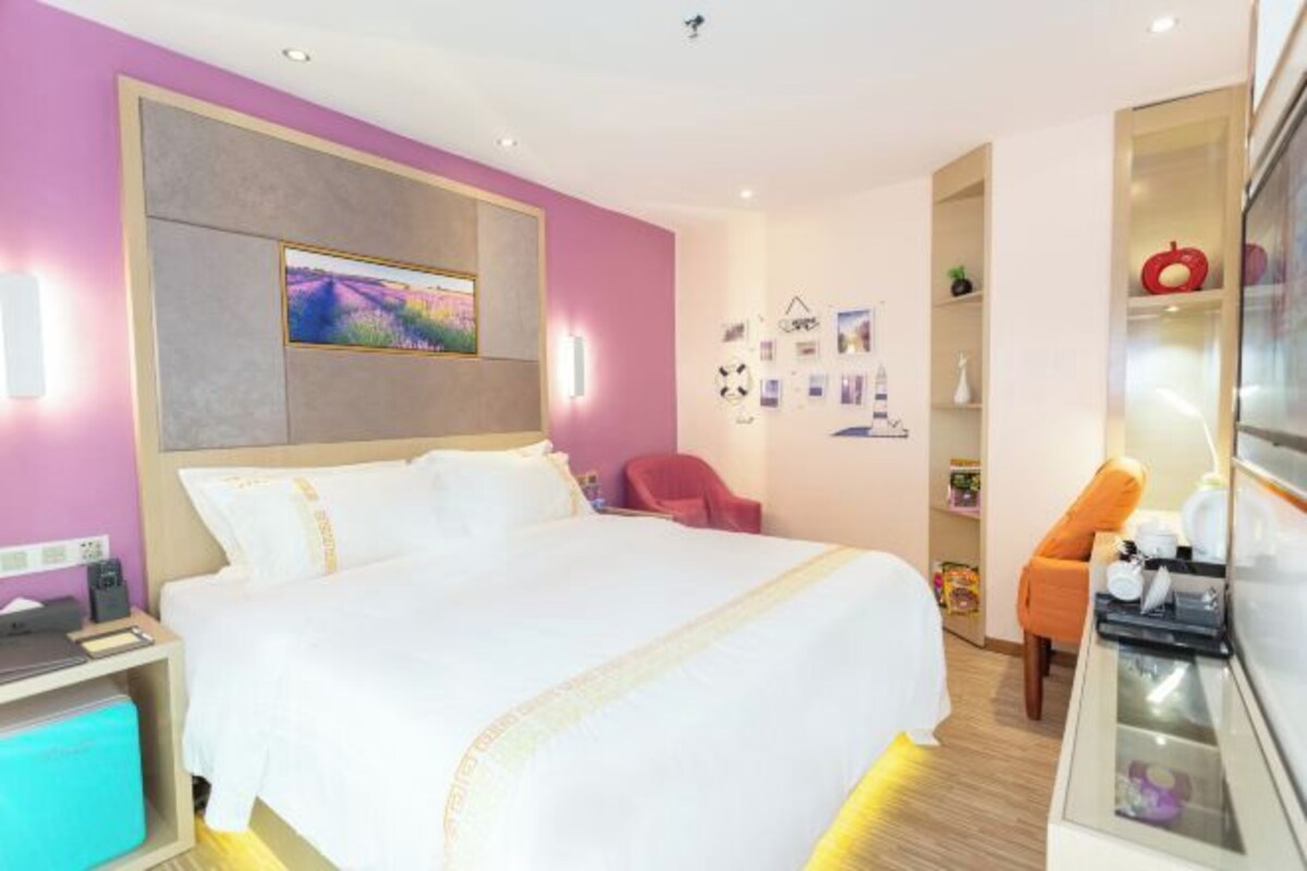 A hotel room with a bed, a desk, a chair, a TV, and a shelf with various items.