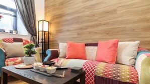 A cozy living room with a wooden floor, a sofa with colorful cushions, a small table with bowls and a plant, and a tall floor lamp. - The Dynar (Helston)