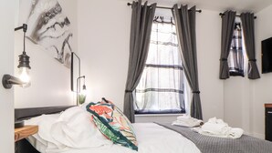 A bedroom with a bed, a window with curtains, a wall-mounted light, and a flat-screen TV. - The Dynar (Helston)