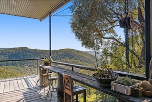 Una terraza de madera con una mesa y sillas, con vista a una ladera boscosa.