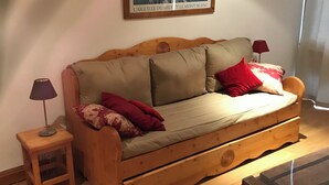 En træsofa med puder, et lille sofabord med lampe, et billede på væggen og et træbord.