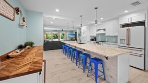 A modern kitchen with a central island, bar stools, and white cabinetry.
