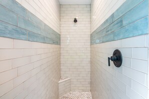 A shower with white and blue tiles, a wall-mounted faucet, and a small step at the bottom. - H2O Bungalow by Beach Boutique Rentals (Anna Maria)