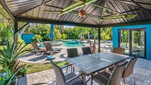 A covered outdoor area with a pool, lounge chairs, and a table.
