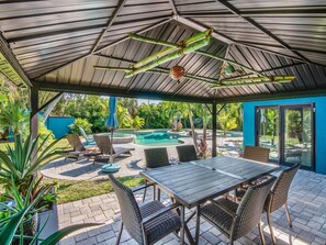 A covered outdoor area with a pool, lounge chairs, and a table.