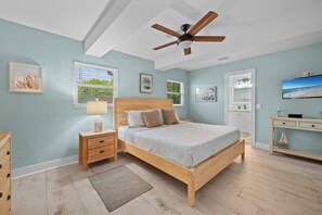 A bedroom with a wooden bed, a nightstand, a desk, a ceiling fan, and a window with blinds.